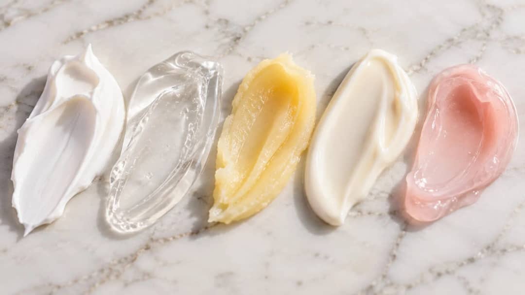 Five Korean moisturizer texture swatches on white marble: rich cream, clear gel, yellow balm, light lotion and pink gel cream