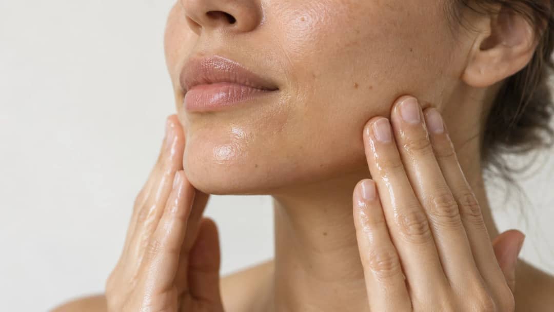 Close up of a woman massaging cleansing oil along her jawline with oil visible on her fingertips