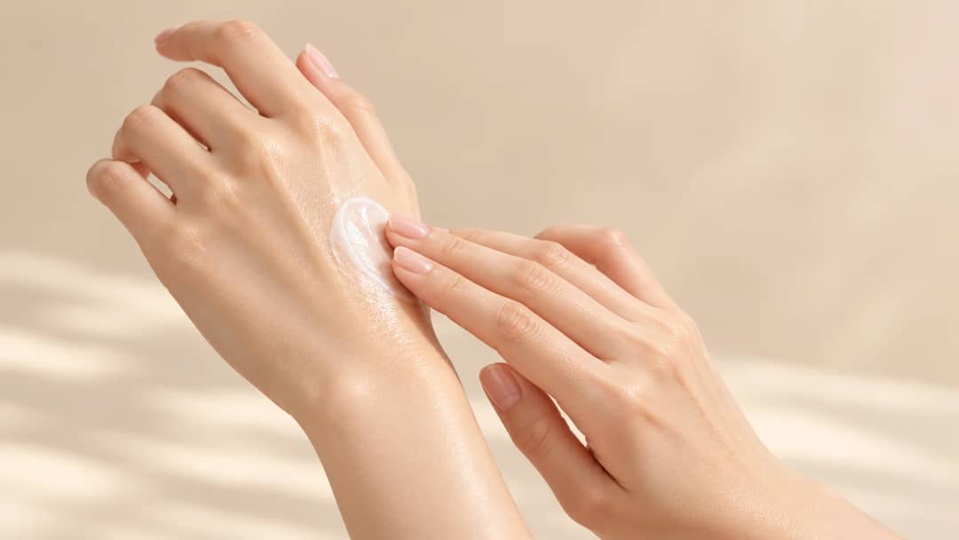 Close-up of hands smoothing sunscreen into the back of a hand, glossy hydrated finish visible