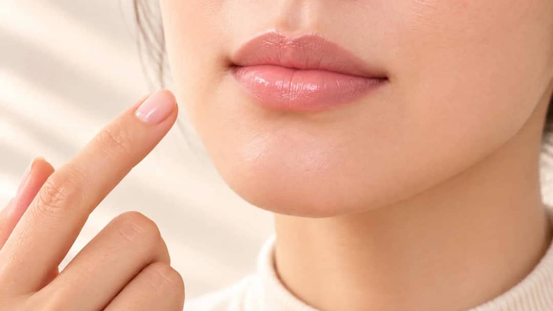Close-up of lips with a thin glossy layer of balm and a fingertip held beside them